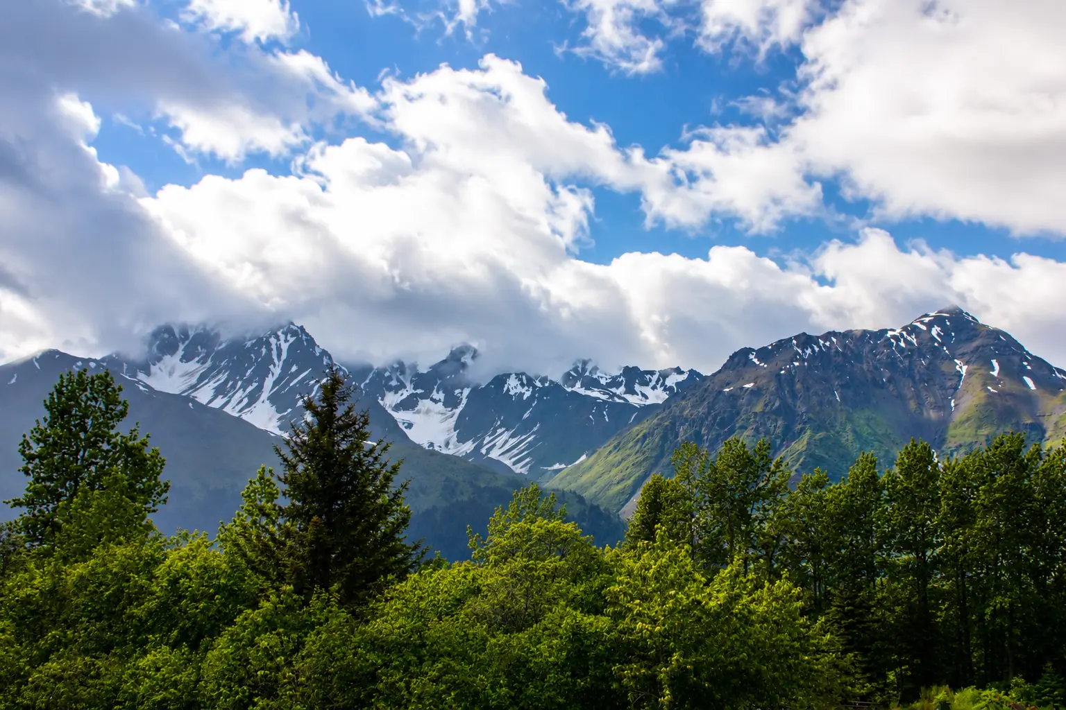 Snow-streaked mountains beneath bright clouds near Resurrection Spa in Seward